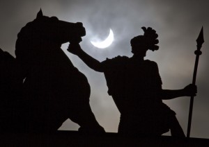 The moon blocks part of the sun during a solar eclipse as seen over a statue at the one of the city landmarks, the General Staff Headquarters in St.Petersburg, Russia, Friday, March 20, 2015. An eclipse is darkening parts of Europe on Friday in a rare solar event that won't be repeated for more than a decade. Credit: AP Photo
