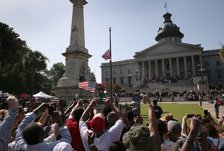 A crowd cheers as a South Carolina state police honor guard lowers the Confederate battle flag from the State House grounds on July 10, 2015, in Columbia, South Carolina. Governor Nikki Haley presided over the event after signing the historic legislation the day before. Credit: © John Moore, Getty Images