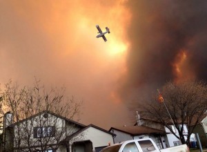 Smoke fills the air as a small plane flies overhead in Fort McMurray, Alberta, Tuesday, May 3, 2016. The entire population of the Canadian oil sands city of Fort McMurray, has been ordered to evacuate as a wildfire whipped by winds engulfed homes and sent ash raining down on residents. Credit: © Kitty Cochrane, The Canadian Press/AP Photos