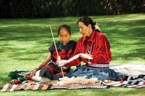 A Navajo woman teaches her daughter how to spin thread for weaving. Many parts of Navajo culture—including the language known as Diné Bizaad—have been passed along from one generation to the next.  In this photograph, a Navajo woman teaches her daughter how to spin thread for weaving. In this way, one part of Navajo culture—the long-held custom of producing richly woven goods such as rugs and blankets—is passed along from one generation to the next. Credit: © Thinkstock