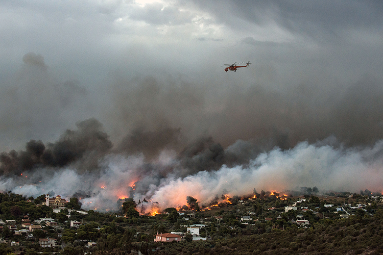 A firefighting helicopter flies over a wildfire raging in the town of Rafina near Athens, on July 23, 2018. - At least five people have died and more than 20 have been injured as wild fires tore through woodland and villages around Athens on Monday, while blazes caused widespread damage in Sweden and other northern European nations. More than 300 firefighters, five aircraft and two helicopters have been mobilised to tackle the "extremely difficult" situation due to strong gusts of wind, Athens fire chief Achille Tzouvaras said.  Credit: © Angelos Tzortzinis, AFP/Getty Images