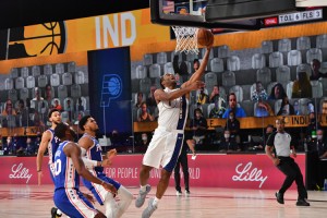 T. J. Warren of the Indiana Pacers goes for a lay-up shot against the Philadelphia 76ers on August 1, 2020, at ESPN's Wide World of Sports at Disney World in Orlando, Florida. The NBA resumed its suspended 2019-2020 season with teams sequestered (isolated) at the resort and no fans in attendance, precautions against the spread of the COVID-19 pandemic (worldwide outbreak of disease). Virtual fans can be seen in the background, projected against the walls of the arena. Credit: © Jesse D. Garrabrant, NBAE/Getty Images