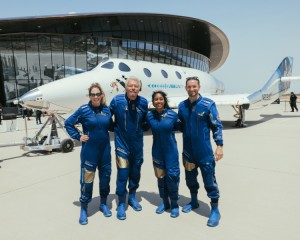 British businessman Richard Branson poses in front of the spaceplane VSS Unity with the other missions specialists of Virgin Galactic’s Unity-22 mission. The glass-paneled terminal of Spaceport America is visible in the background. From left to right: Beth Moses, Chief Astronaut Instructor; Branson; Sirisha Bandla, Vice President of Government Affairs and Research Operations; Colin Bennett, Lead Operations Engineer. Credit: © Virgin Galactic