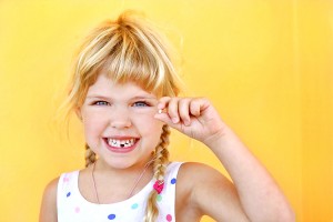 A child smiles holding a missing baby tooth. Credit: © Yaroslav Mishin, Shutterstock